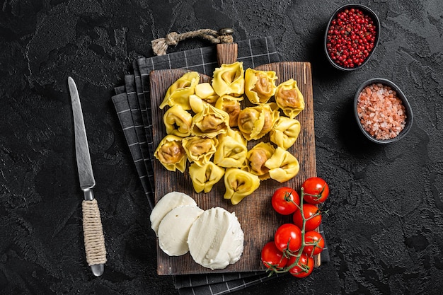 Preparação de ravióli cru com queijo mussarela e tomate. fundo preto. vista do topo.