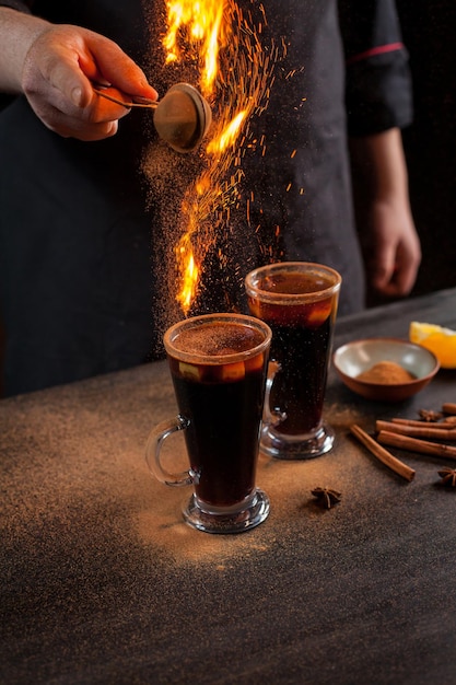 Preparação de vinho quente para servir, em restaurante. vinho quente na preparação do bar do chef. as mãos do chef em um fundo escuro e preto. vinho quente quente com faíscas.