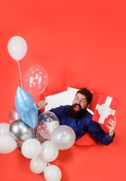 Preparação para a festa de aniversário. Homem sorridente, olhando pelo buraco do papel, segurando balões e uma festa de presente