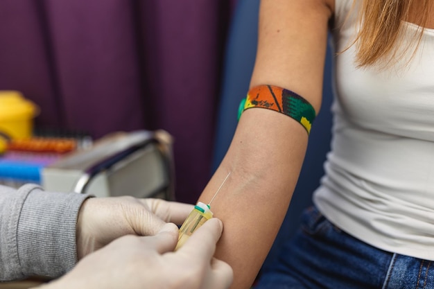 Preparação para exame de sangue com bela jovem pelo uniforme médico feminino em cima da mesa na sala branca brilhante Enfermeira perfura a veia do braço do paciente com tubo em branco de agulha