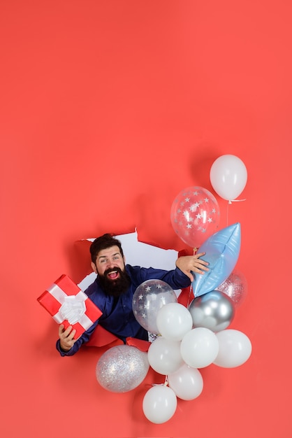 Preparação para festa de aniversário elegante homem barbudo com balões infláveis segurando caixa de presente sorrindo