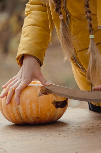 Preparação para o Halloween: menina cortando abóbora. Fechar-se. Conceito de decoração de férias. Mulher prepara jack-o-lantern. Festa de decoração. Ajudante pequeno.