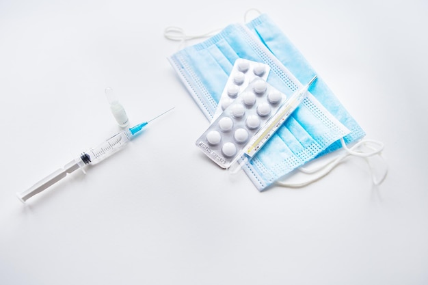 Preparação para vacinação contra covid19 Pílulas de termômetro máscara médica em uma mesa branca Lugar para uma foto horizontal de inscrição