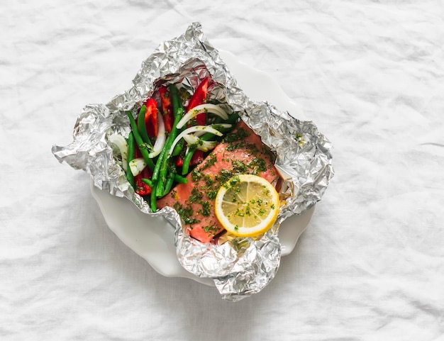 Preparación del almuerzo salmón al horno con frijoles, pimienta roja dulce y salsa de pesto en papel de aluminio en un fondo claro vista superior