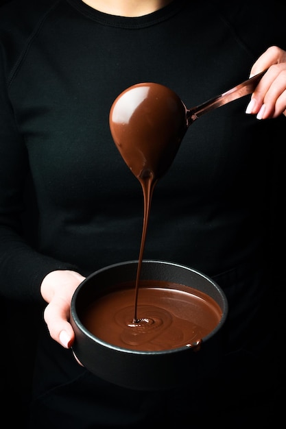 Preparación de chocolate derretido en manos de un chocolatero Batidor de cocina Sobre fondo negro