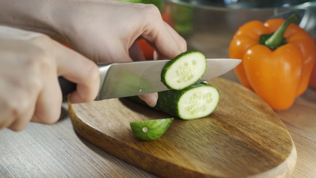Foto preparación de ensalada de verduras cortadas en un picado de madera manos de las mujeres cortan pepino grande k video