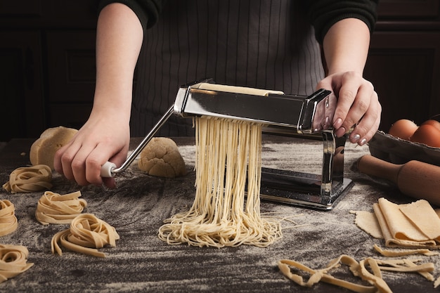 Preparación de fettuccine casero en máquina de pasta. Cortar la masa cruda en tallarines en un equipo especial, concepto de cocina tradicional italiana, espacio de copia