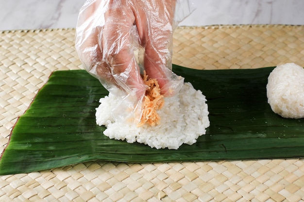 Preparación para hacer Lemper Ayam, refrigerio tradicional de Indonesia hecho con arroz pegajoso al vapor, relleno de pollo desmenuzado y envuelto con hoja de plátano