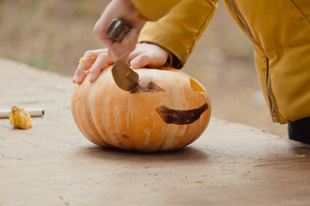 Preparación para Halloween: niña cortando calabaza. De cerca. Concepto de decoración de vacaciones. Mujer prepara jack-o-lantern. Fiesta de decoración. Pequeño ayudante.