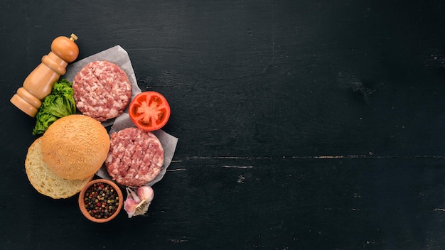 Preparación de hamburguesa Carne verduras frescas tomates cebollas Sobre un fondo de madera negra Vista superior Espacio de copia libre