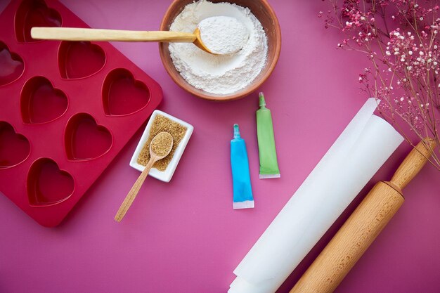 Preparación para hornear molde de silicona en forma de corazón rodillo confitería jeringa glaseado harina azúcar sobre fondo rosa Concepto del día de San Valentín Foto de alta calidad