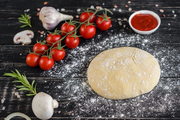 Preparación de la masa y hortalizas para producción de pizza. Ingredientes para la producción de pizza sobre un fondo de madera.