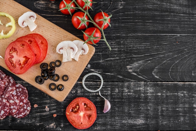 Preparación de la masa y hortalizas para producción de pizza. Ingredientes para la producción de pizza sobre un fondo de madera.