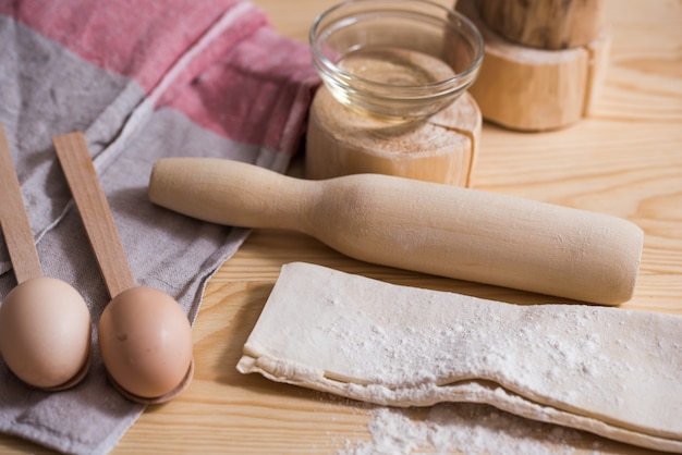 Preparación de la masa. Ingredientes para la masa - Huevos y harina con un rodillo. Sobre fondo de madera