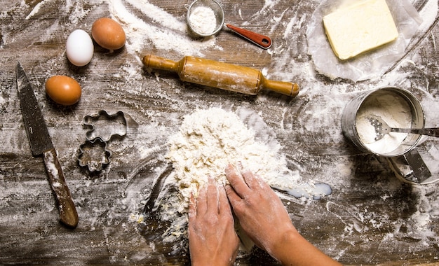 Preparación de la masa. Las manos y las herramientas de las mujeres de masa: colador, rodillo, cuchillo, batidor. Sobre una mesa de madera. Vista superior