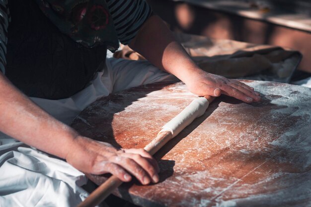 Preparación de la masa. La masa rodando por las manos de las mujeres con harina de rodillo en d de madera