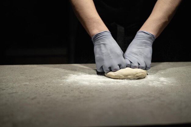 Preparación de masa de pizza. Manos de panadero masculino con guantes de goma amasan masa para pizza italiana en la mesa de trabajo. Proceso de horneado.