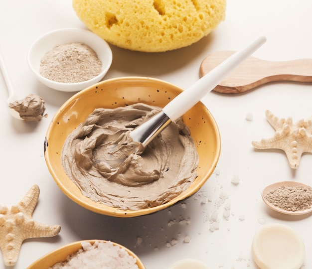 Preparación de mascarilla de barro cosmético en cuenco de cerámica sobre fondo blanco. Primer plano de la textura de la emulsión de arcilla facial. Cosmética natural para tratamientos de spa en el hogar o en el salón.