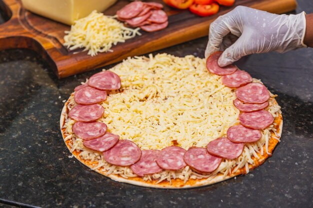 Preparación de pizza extendiendo anillos y rebanadas de pepperoni sobre masa de pizza Ingredientes frescos de pizza sobre tabla de madera