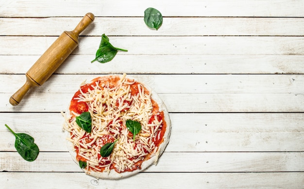 Preparación de pizza con varios ingredientes. Sobre una mesa de madera blanca.