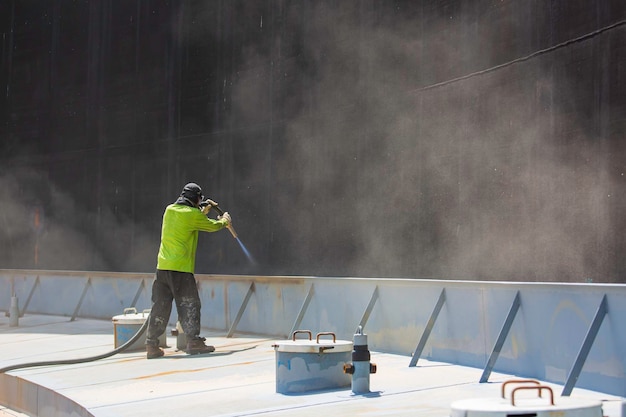 Preparación de la placa de corrosión de la superficie del trabajador masculino mediante chorro de arena del pontón de la cubierta superior del tanque