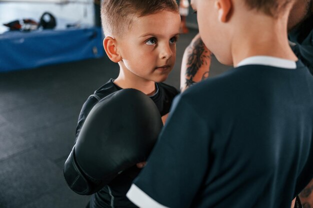 Preparación previa a la pelea Mirándose el uno al otro Entrenador tatuado joven enseñando a los niños técnicas de boxeo