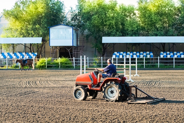 Preparación de la ruta en la pista de carreras: el tractor alinea el suelo. un jinete en un caballo cabalga cerca. deportes ecuestres, carreras de caballos, apuestas