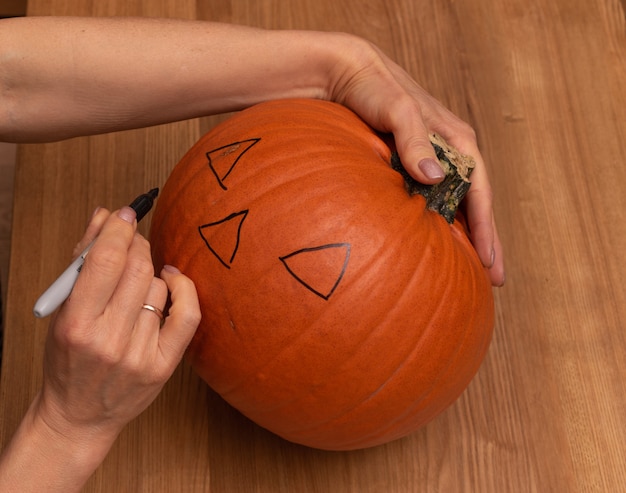 Foto preparaciones para halloween, manos de mujer haciendo bocetos en calabaza.