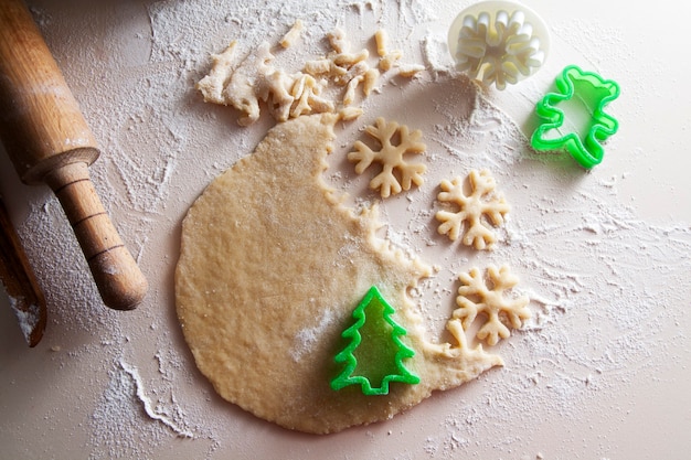 Preparaciones navideñas: galletas caseras en forma de árbol de Navidad y copos de nieve. Masa enrollada sobre la mesa y cortadores, rodillo. Humor navideño, hornear, familia, concepto de hogar