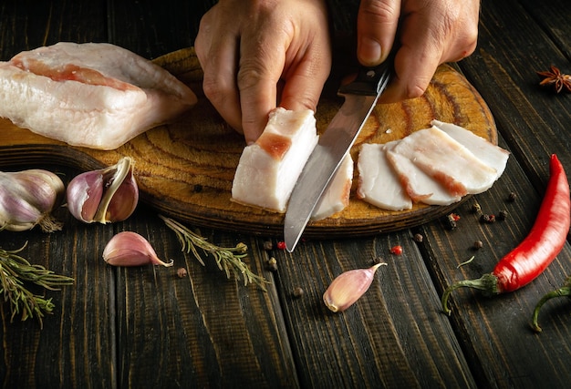 Preparamos sanduíches para um lanche ou refeição rápida de banha e alho as mãos dos cozinheiros cortam banha de porco com uma faca em uma tábua de corte de madeira comida camponesa