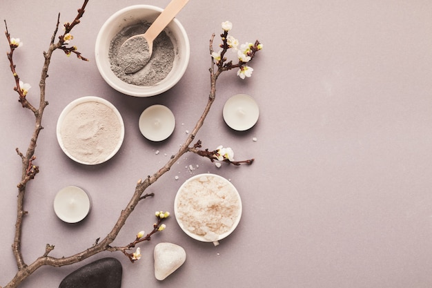 Preparando a máscara de lama preta cosmética em fundo cinza com flor tenra. Cosméticos naturais para tratamento de spa em casa ou em salão de beleza, vista de cima, espaço de cópia