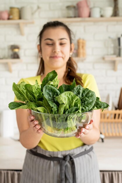 Preparando alimentos saudáveis Alimentação e dieta saudáveis Jovem morena caucasiana segurando uma tigela de espinafre fresco na cozinha