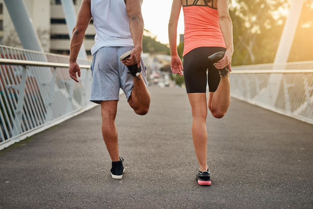 Preparando as pernas para uma corrida Foto retrospectiva de um jovem casal se aquecendo em uma ponte antes do treino