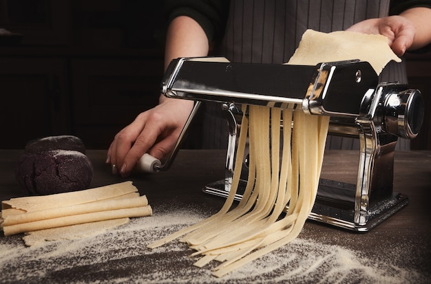 Preparando fettuccine caseiro na máquina de macarrão. Corte a massa crua em tagliatelle em equipamento especial, conceito tradicional de cozinha italiana, copie o espaço