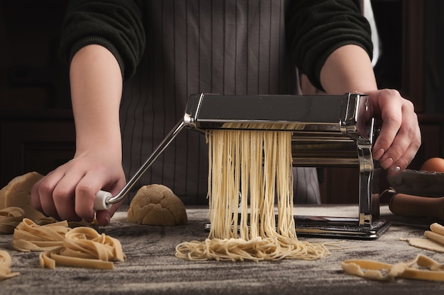 Preparando fettuccine caseiro na máquina de macarrão. Corte a massa crua em tagliatelle em equipamento especial, conceito tradicional de cozinha italiana, copie o espaço