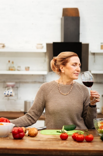 Preparando o jantar. Mulher tranquila e bonita com cabelo amarrado em uma noite tranquila tomando vinho tinto