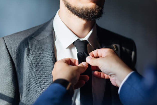 Preparando os noivos para a manhã noivo bonito se vestindo e se preparando para o casamento camisa branca Um amigo endireita a gravata de um homem