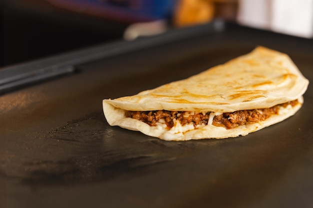 Preparando quesadilla fresca en una parrilla negra en el mercado de alimentos local