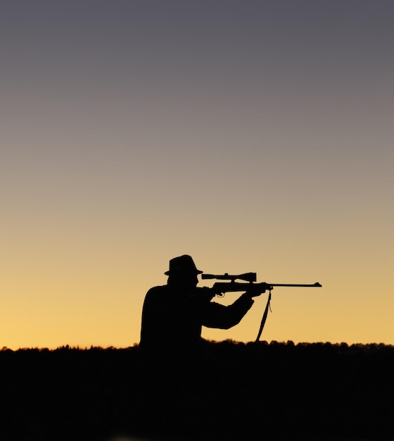 Preparando-se para atirar Uma silhueta de um homem ao ar livre segurando seu rifle sniper