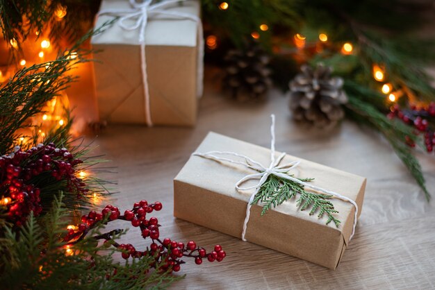 Preparando-se para o feriado em casa, presente de Natal embrulhado em papel artesanal em uma mesa de madeira com decoração e luzes de guirlanda.
