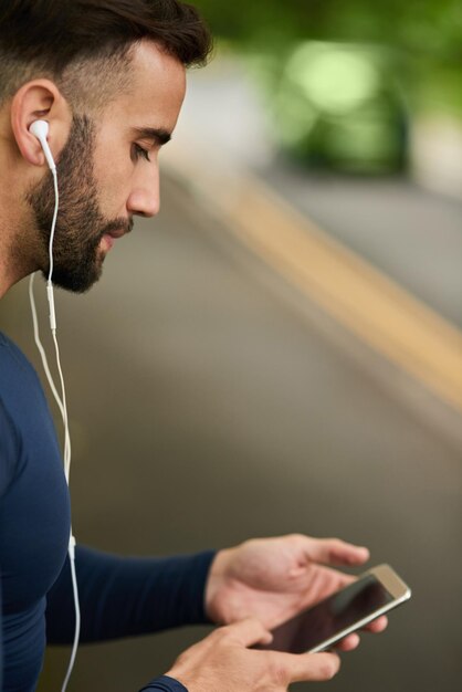 Preparando su lista de reproducción de entrenamiento Captura recortada de un apuesto joven corredor revisando sus mensajes durante su entrenamiento