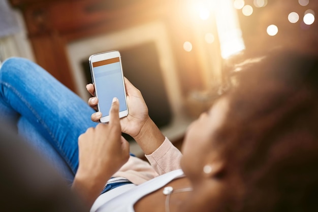 Preparando sus planes de fin de semana Toma en ángulo alto de una joven irreconocible usando su celular mientras se relaja en el sofá de su casa