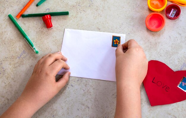 Preparándonos para el día de Valentin. Tema del día de San Valentín. Concepto de artesanía. Niño poniendo corazón rojo