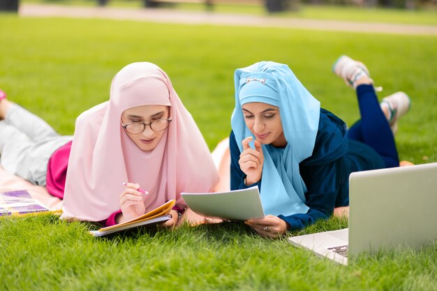 Preparándose para el examen. Dos estudiantes musulmanes inteligentes sentados en el césped y preparándose para el examen juntos