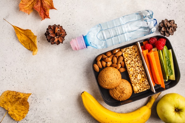 Preparar alimentos saludables en recipientes para la escuela con barra de cereal, frutas, verduras y bocadillos. Comida para llevar en el fondo blanco, vista superior.