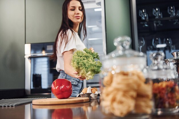 Preparar alimentos usando verduras y productos saludables Morena hermosa joven con ropa informal en el interior de la cocina durante el día