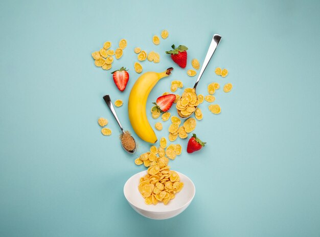 Preparar un desayuno rápido y saludable por la mañana: agregar cereales, plátano maduro, fresa fresca en un tazón blanco. Ingredientes para hacer el desayuno con granola y frutas sobre fondo azul, vista superior