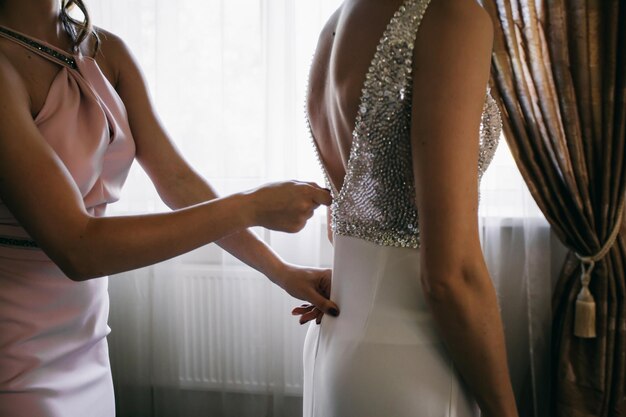 preparativos para a noiva pela manhã, damas de honra amarrando um vestido com as costas abertas para a noiva.