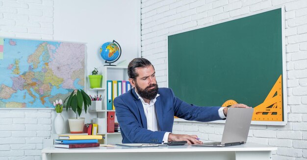 Prepare-se para o exame online. professor universitário na lição. de volta à escola. educação não formal. professor maduro sério trabalhando no laptop. homem barbudo brutal trabalha em sala de aula com computador.