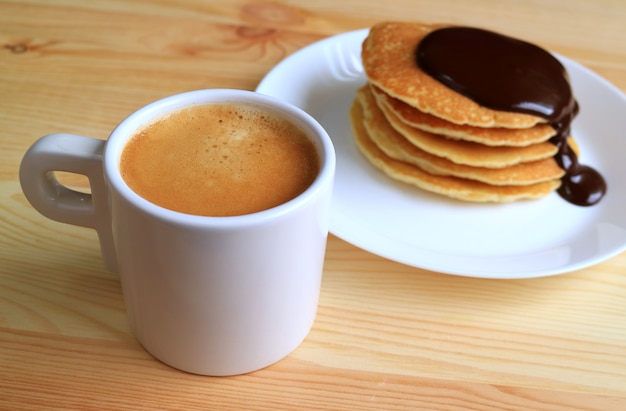 Prepare uma xícara de café quente com panqueca desfocada com molho de ganache de chocolate no fundo